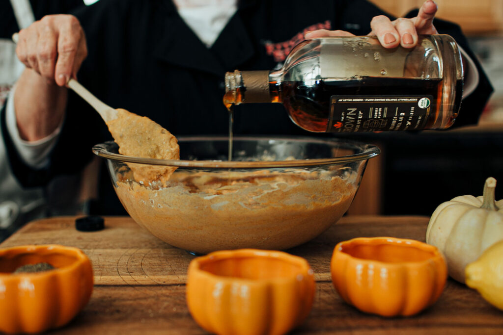 Batter being poured into a bowl on the counter, small pumpkins beside it